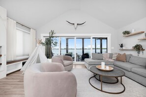 A spacious living room with a large window, a white ceiling, and a view of the water.