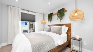 A bedroom with a bed, a bedside table, a hanging plant, and a window with curtains. - Roxie's Modern Lake Front House on the water! (Russells Point)