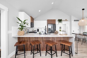 A modern kitchen with white cabinets, a stainless steel refrigerator, and wooden stools.