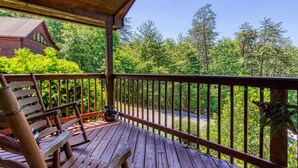 Une terrasse en bois avec un banc et une table, donnant sur une zone boisée sous un ciel dégagé.