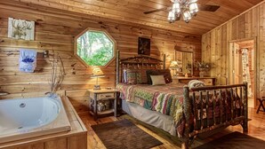 Une chambre confortable dans un chalet, avec un grand lit, un plafond en bois, une fenêtre, un ventilateur de plafond et une baignoire.