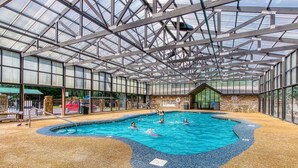 Une piscine intérieure dotée d’un toit en verre, entourée d’un sol en galets et adossée à un mur de pierre.