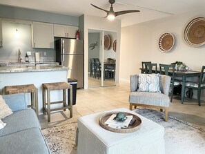A modern kitchen with a built-in refrigerator, a dining area with a green table and chairs, and a living room with a gray sofa and a patterned ottoman. - Beautiful, totally remodeled 1 bedroom, 2 full bathroom condo just steps to the beach! (Ocean City)