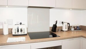 A modern kitchen with white cabinets, a black induction cooktop, a kettle, and a toaster. - TMS Beautiful 2BR Apartment! Ensuite! Lakeside (Grays)