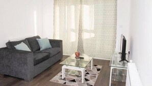 A modern living room with a grey sofa, a glass coffee table, and a TV on a stand. - TMS Beautiful 2BR Apartment! Ensuite! Lakeside (Grays)