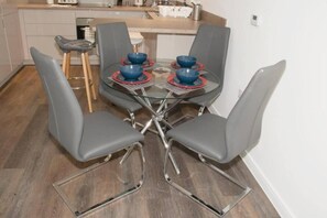 A modern kitchen with a round glass table, four grey chairs, and blue bowls on red coasters.