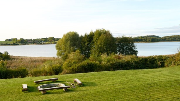A grassy field with a lake, trees, and a bench. - House (Klein Upahl)