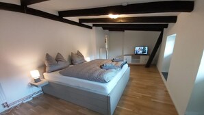 A bedroom with a large bed, a bedside table with a lamp, and a television in the corner. - House (Klein Upahl)