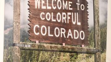 Segnaletica in legno con la scritta 'WELCOME TO COLORFUL COLORADO' sullo sfondo di una foresta e montagne.