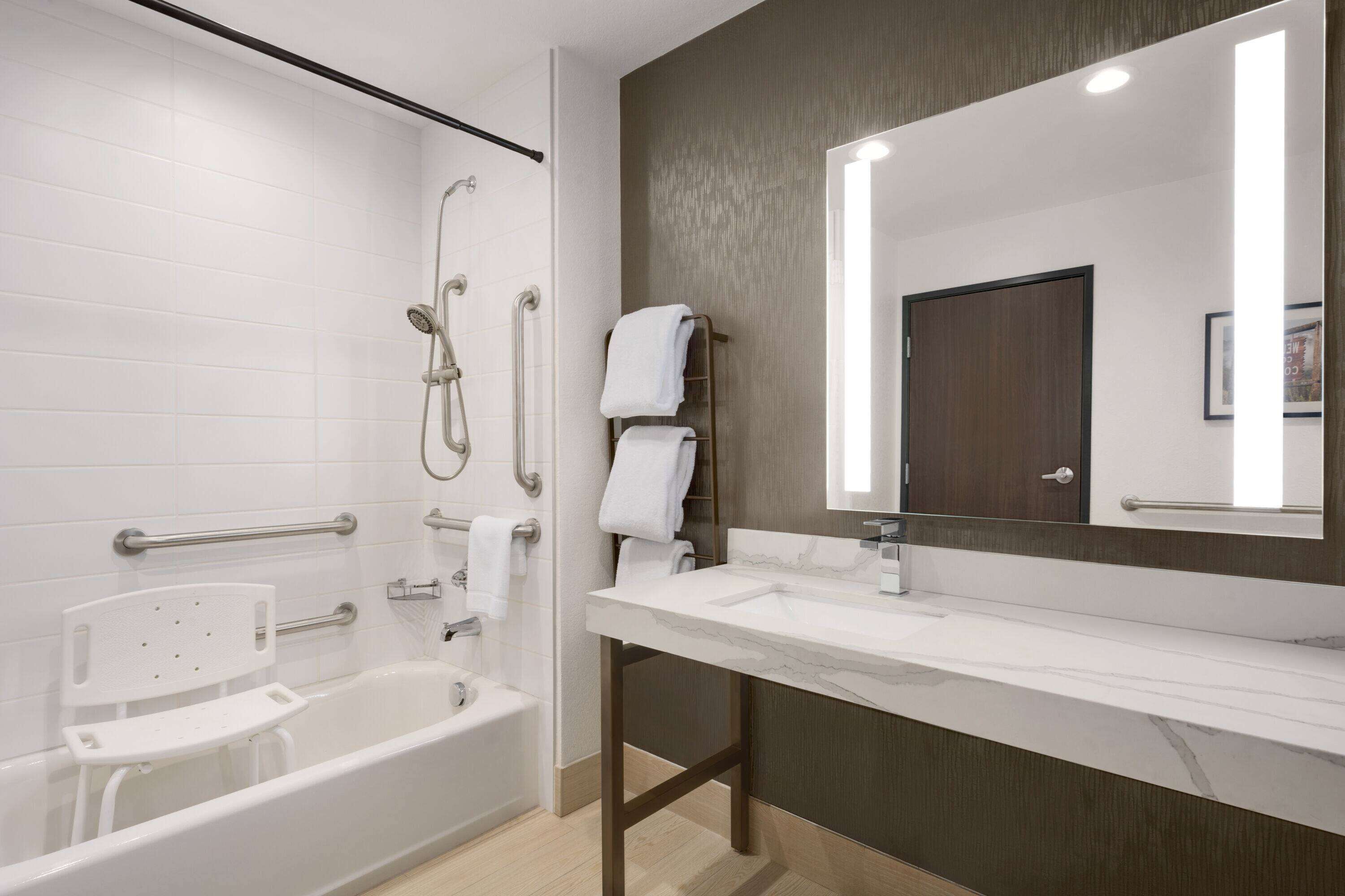 A modern bathroom with a bathtub, shower, and vanity with a large mirror.