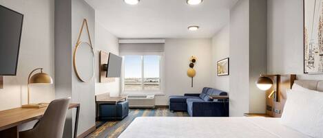 Une chambre d’hôtel avec un grand lit, un bureau avec une chaise, un canapé, une télévision et une fenêtre donnant sur un beau paysage.