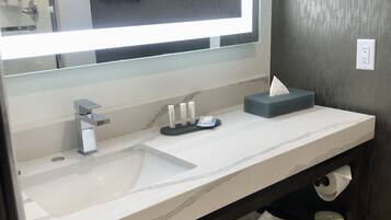 A bathroom with a large mirror, two sinks, a towel rack with folded towels, and a framed picture on the wall.