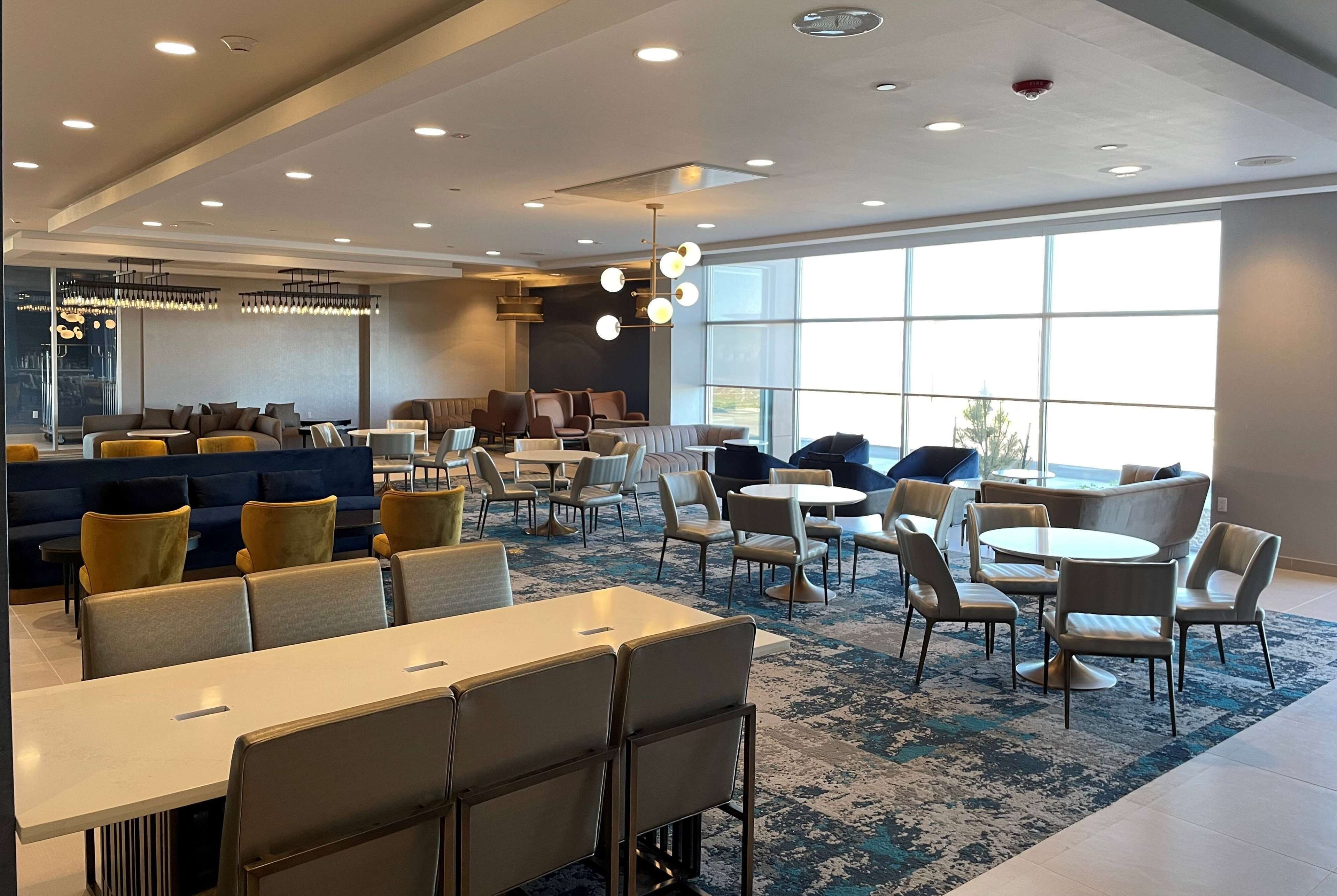 A modern hotel lobby with seating areas, a bar, and large windows providing natural light.