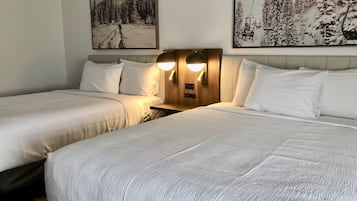 A hotel room with two beds, a wooden headboard with wall-mounted lights, and two framed pictures depicting snowy landscapes.