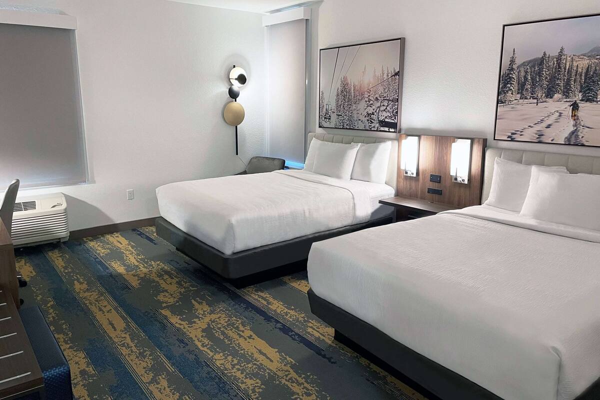 Hotelkamer met twee bedden, een groot raam, een wandlamp en een schilderij met ski-thema.