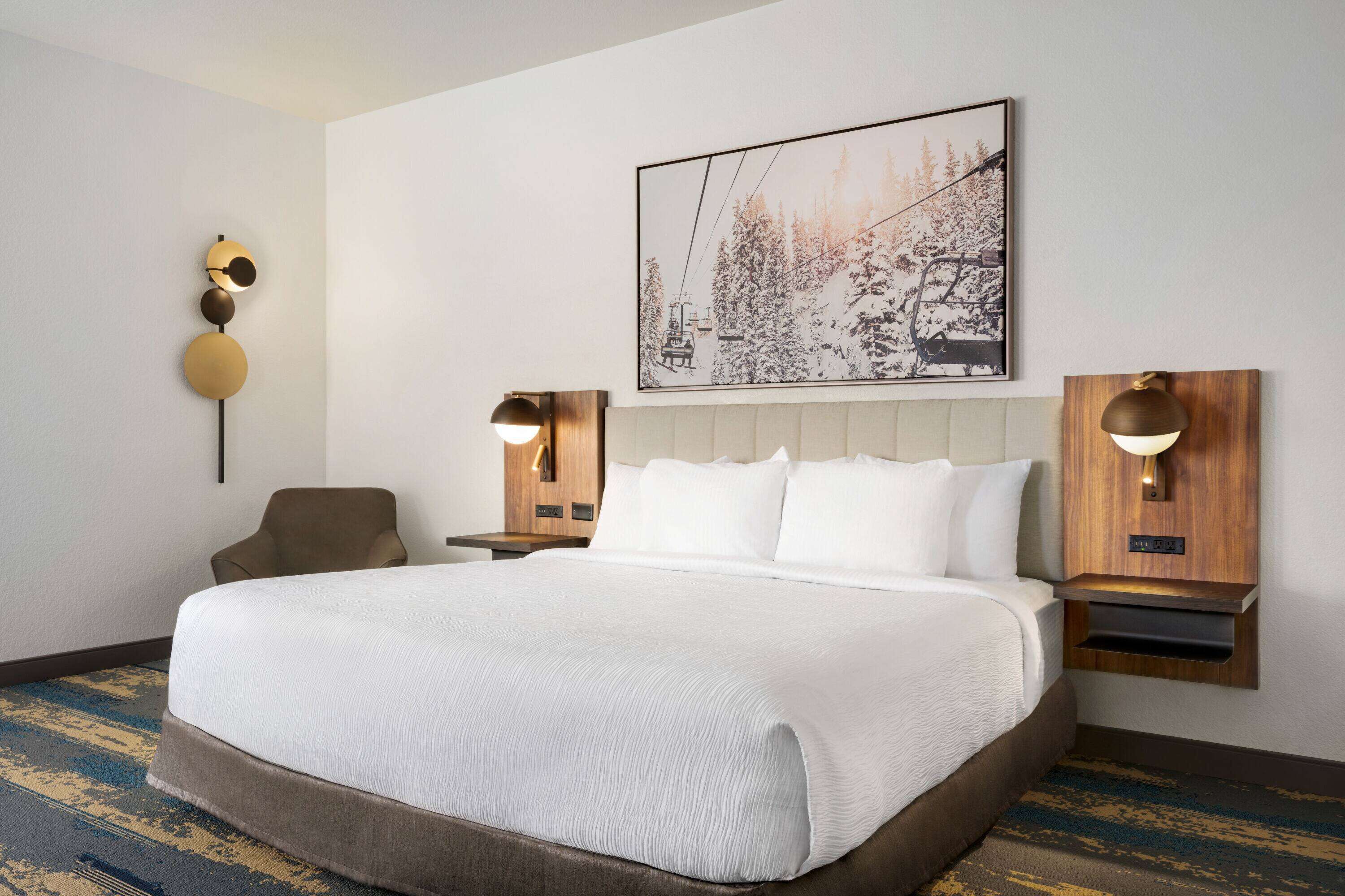 A hotel room with a large bed, two bedside tables with lamps, a chair, and a framed picture on the wall.