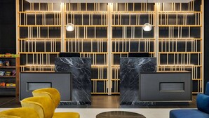 Un área de recepción con diseño moderno, que cuenta con un mostrador de mármol, asientos cómodos y una pared decorativa con paneles iluminados.