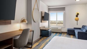 Habitación de hotel con cama, escritorio, silla y televisor en la pared.