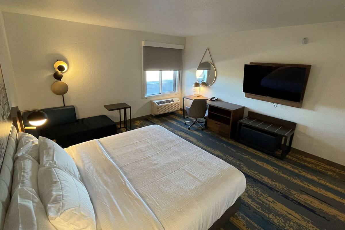 Een hotelkamer met een groot bed, een bureau met stoel, een televisie, een raam met uitzicht en een spiegel aan de muur.
