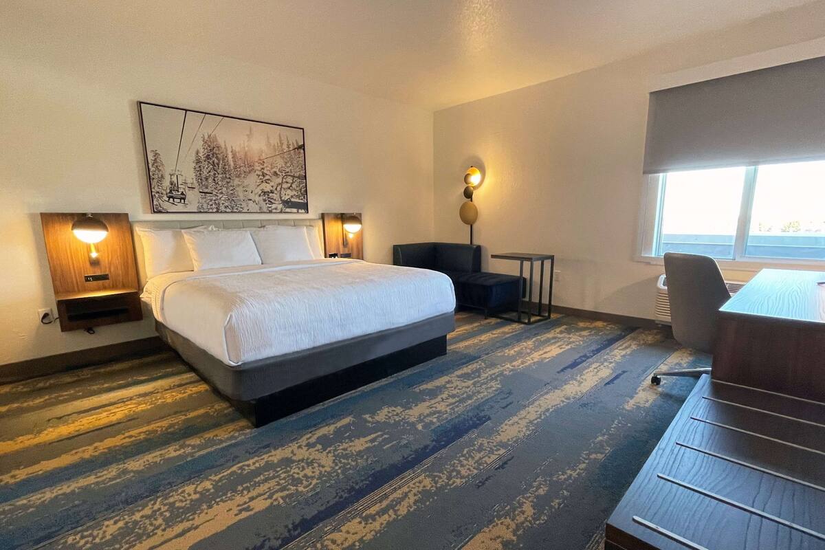 Een hotelkamer met een groot bed, twee nachtkastjes met lampen, een bureau, een stoel en een raam met uitzicht.