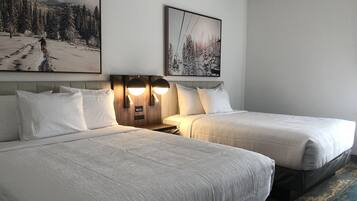 Habitación de hotel con dos camas, un cabecero con iluminación integrada y dos cuadros en la pared.