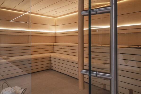 Un sauna moderno y bien iluminado con bancos de madera y separaciones de vidrio.