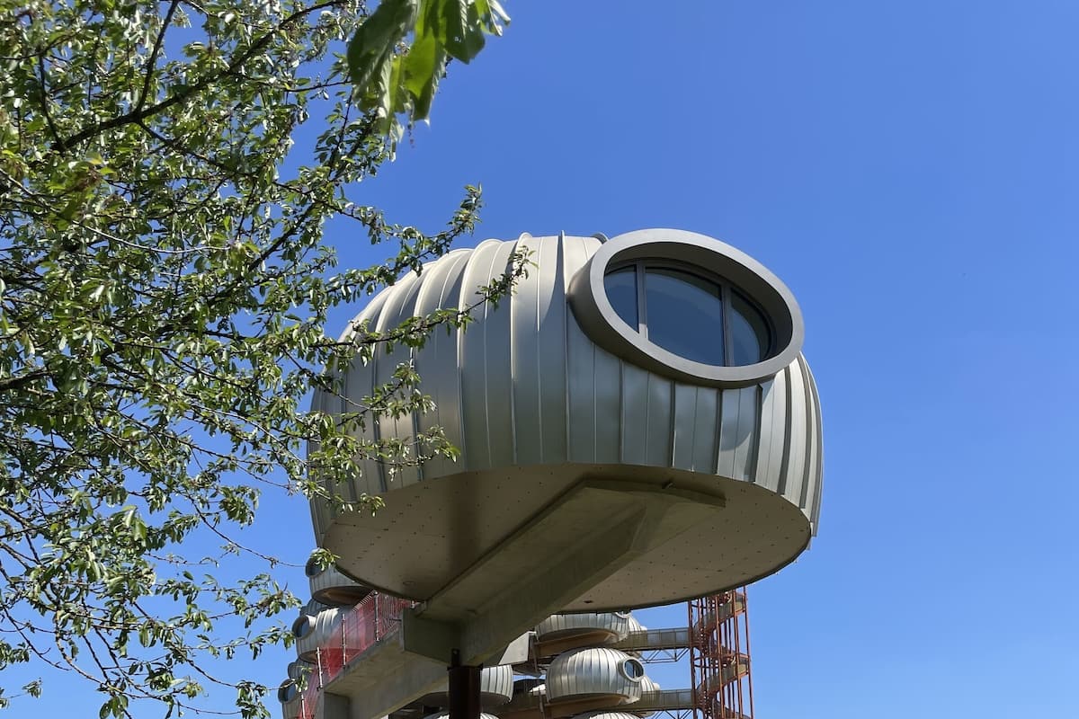 A modern building with a unique circular design, surrounded by a grassy field and a stone wall.