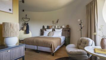 A modern bedroom with a bed, bedside table, lamp, chair, and a small table with a book.