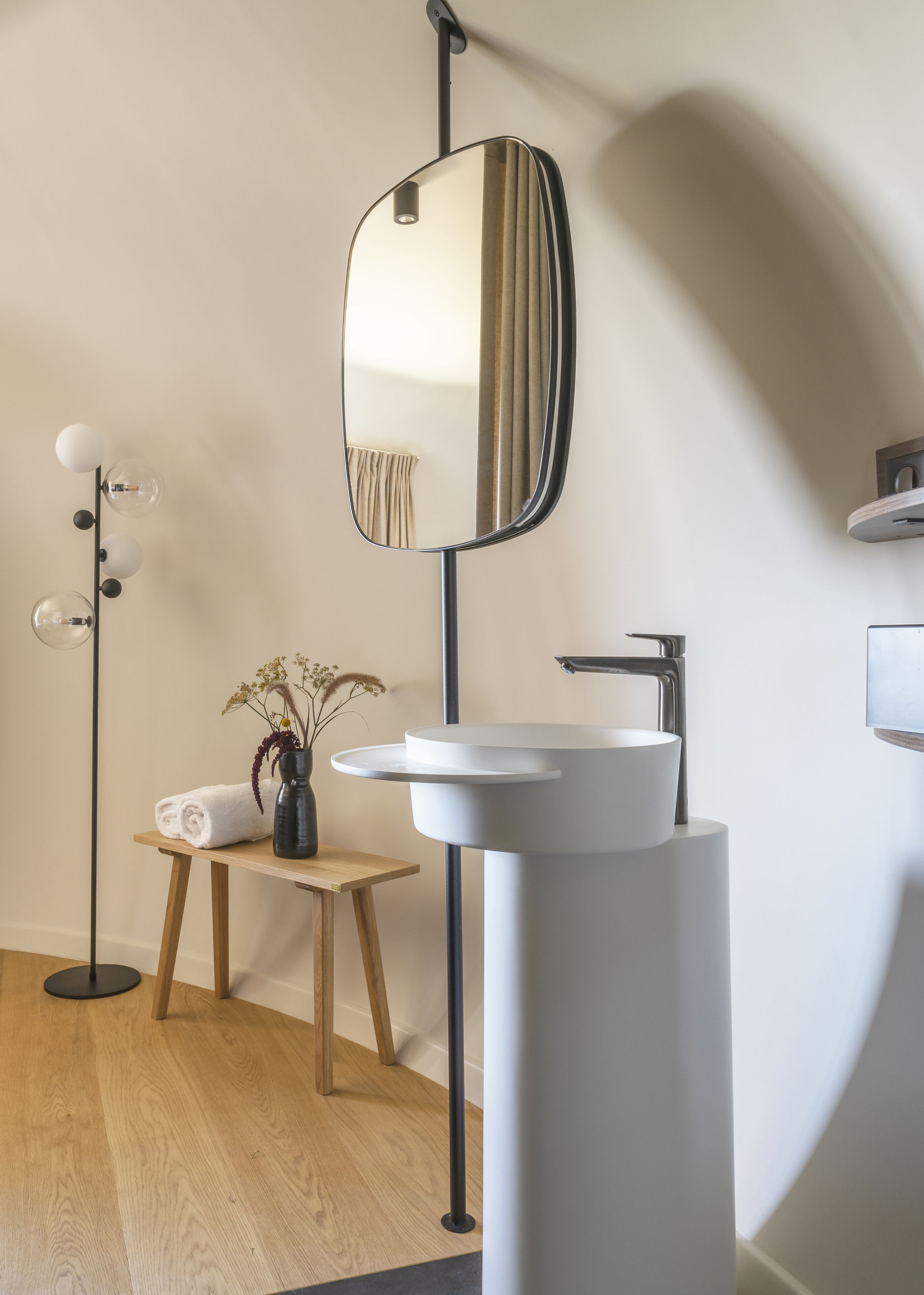 Un baño moderno con un espejo redondo, un lavabo blanco y una lámpara de pie.