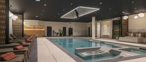 Een modern binnenzwembad met loungebedden en een geometrisch lamp.