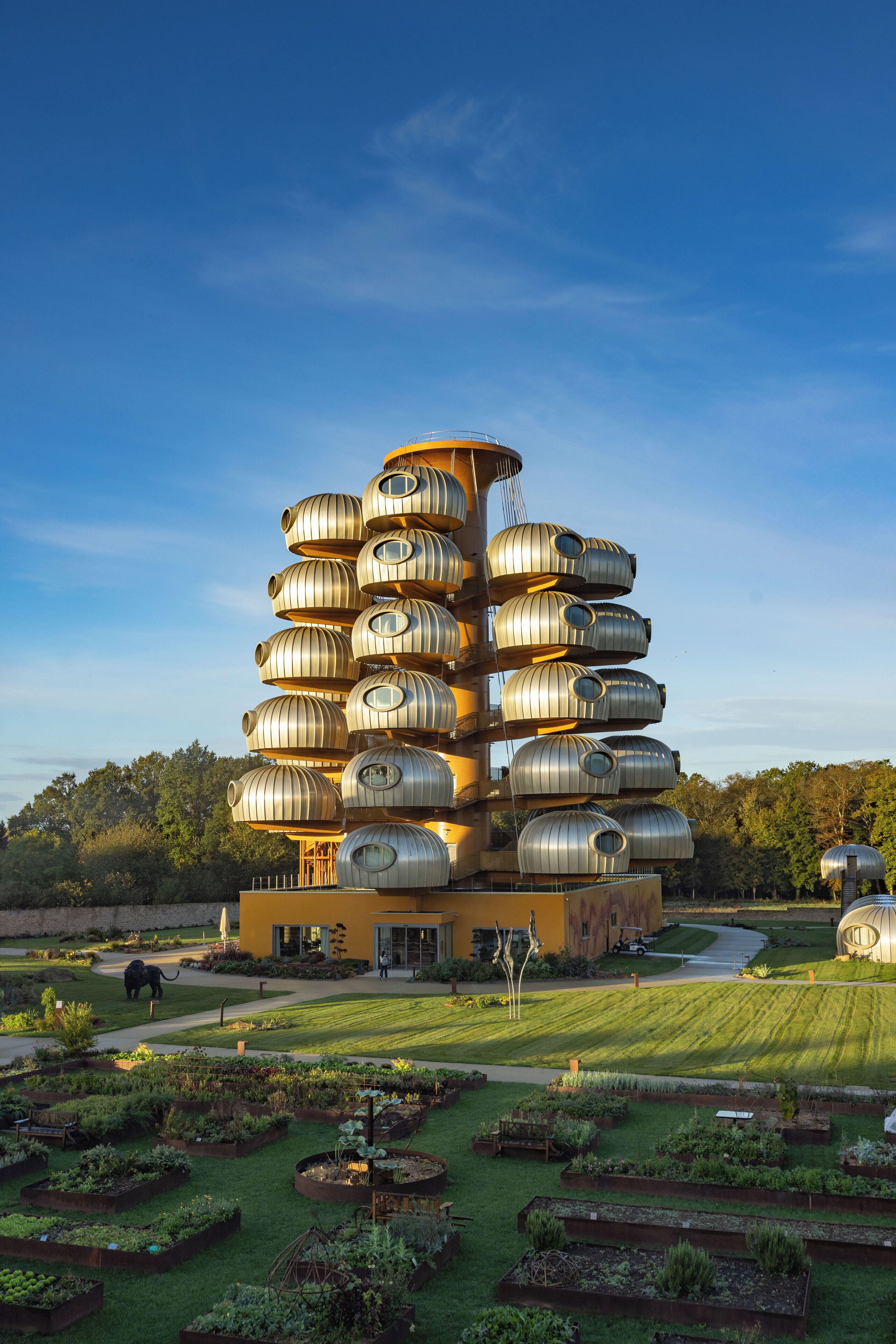 A unique multi-level cylindrical building with a central staircase, surrounded by a well-maintained garden with various plants and a pathway.