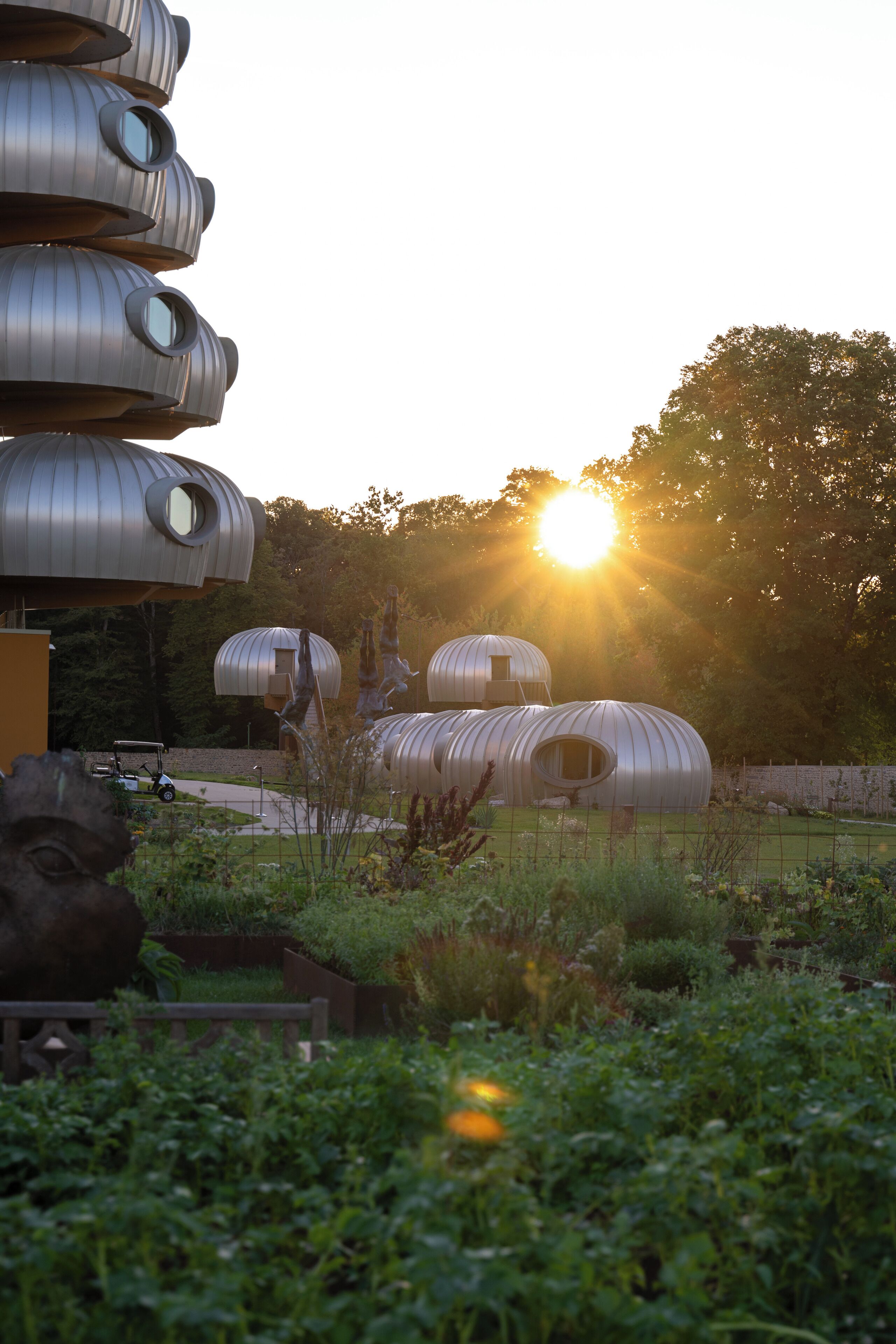 A series of cylindrical metal structures with circular windows, surrounded by greenery and a golf cart in the background.