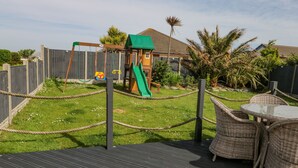 A wooden deck with a rope fence, a green slide, and wicker furniture. - Aurora (Holyhead)