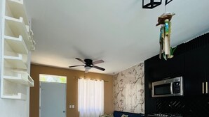 A compact living space with a dining area featuring a round table and four chairs, a kitchenette with modern appliances, a ceiling fan, and a decorative plant. - Private Pool, Modern 2 bedroom Villa (Juan Dolio)
