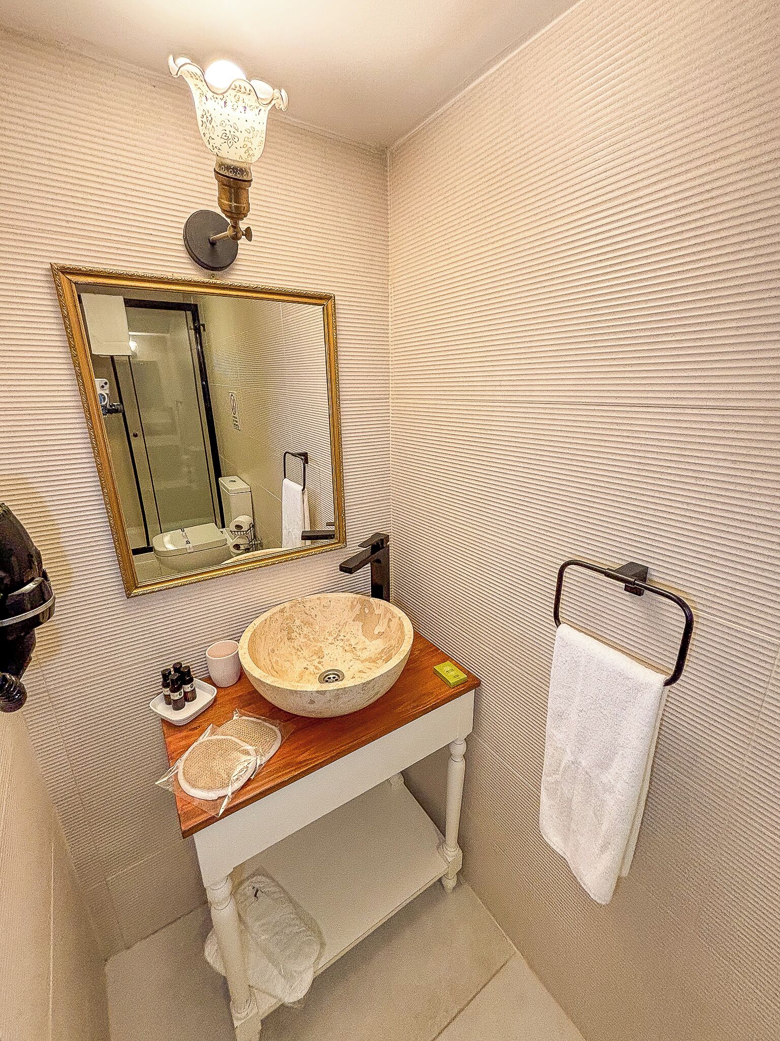 A bathroom with a wooden vanity, a large mirror, a towel rack, and a wall-mounted light fixture.