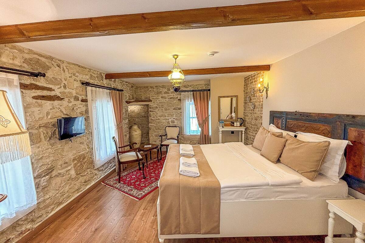 A bedroom with a bed, a television, a stone wall, and a wooden ceiling.