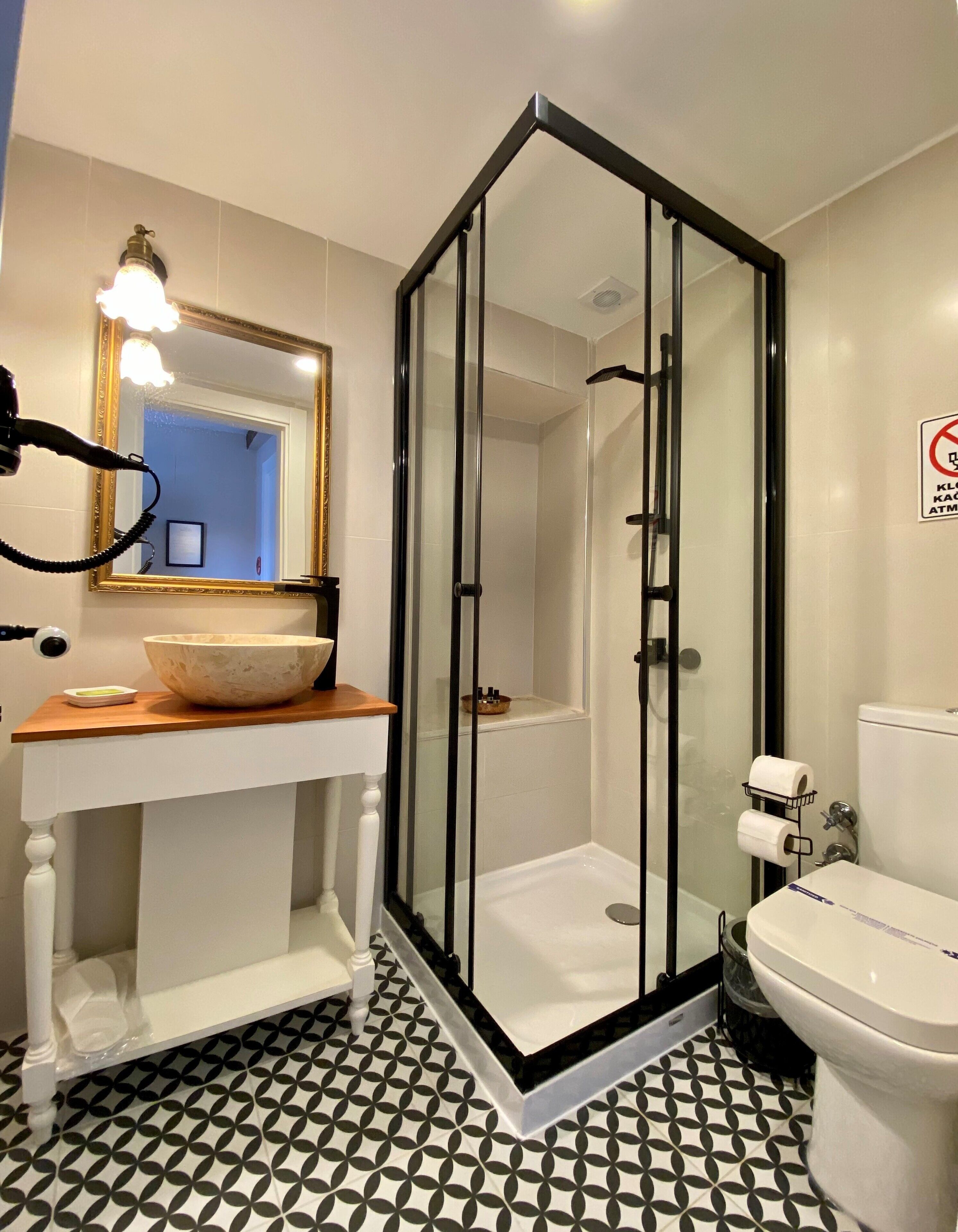 Un baño moderno con ducha envuelta en vidrio, un lavabo blanco con un recipiente decorativo y un inodoro.