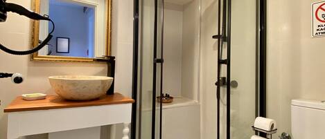 Un baño moderno con ducha envuelta en vidrio, un lavabo blanco con un recipiente decorativo y un inodoro.