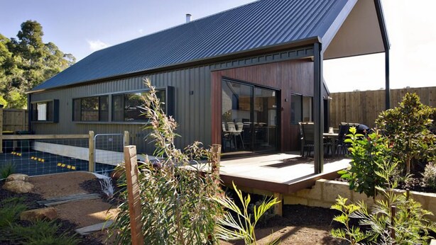 A modern house with a large deck, a swimming pool, and a fenced garden area.