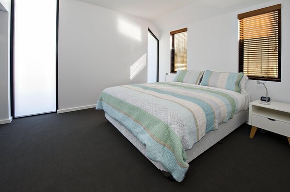 A bedroom with a bed, a bedside table, and a window with blinds.