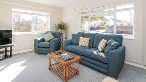 A modern living room with a sofa, armchair, and a glass coffee table. - Sunnyside (Wells-next-the-Sea)