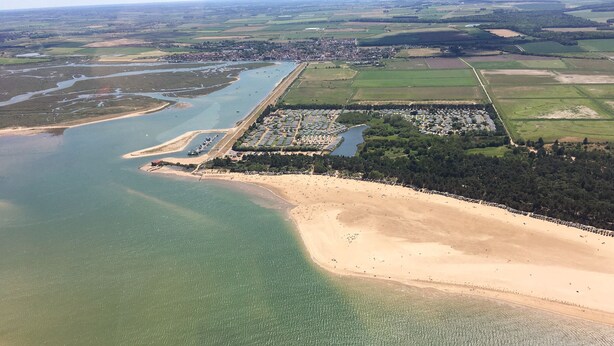 An aerial view of a coastal area with a sandy beach, a marina, and a residential area with houses and greenery. - Sunnyside (Wells-next-the-Sea)