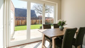 A dining area with a table and chairs, a vase of flowers, and a sliding glass door leading to a backyard. - Sunnyside (Wells-next-the-Sea)