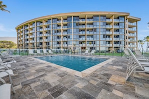 Un hotel de varios pisos con una piscina rodeada de sillones de descanso.