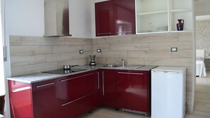 A compact kitchen with red cabinets, a white refrigerator, and a built-in stove. - Adriana House ground floor with enchanting lake view (Bee)