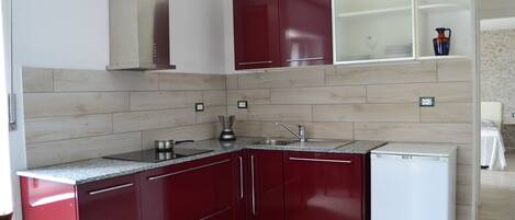 Cocina compacta con armarios rojos, refrigerador blanco y estufa integrada.