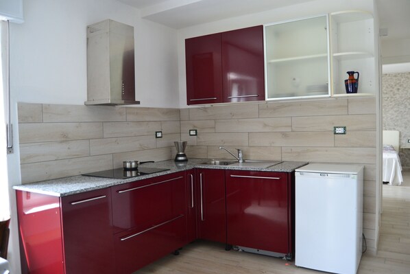 Cocina compacta con armarios rojos, refrigerador blanco y estufa integrada.