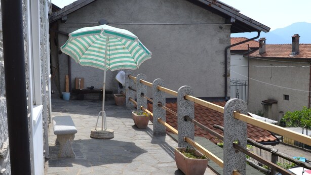 A stone-paved terrace with a green and white striped umbrella, a stone bench, and potted plants. - Adriana House ground floor with enchanting lake view (Bee)