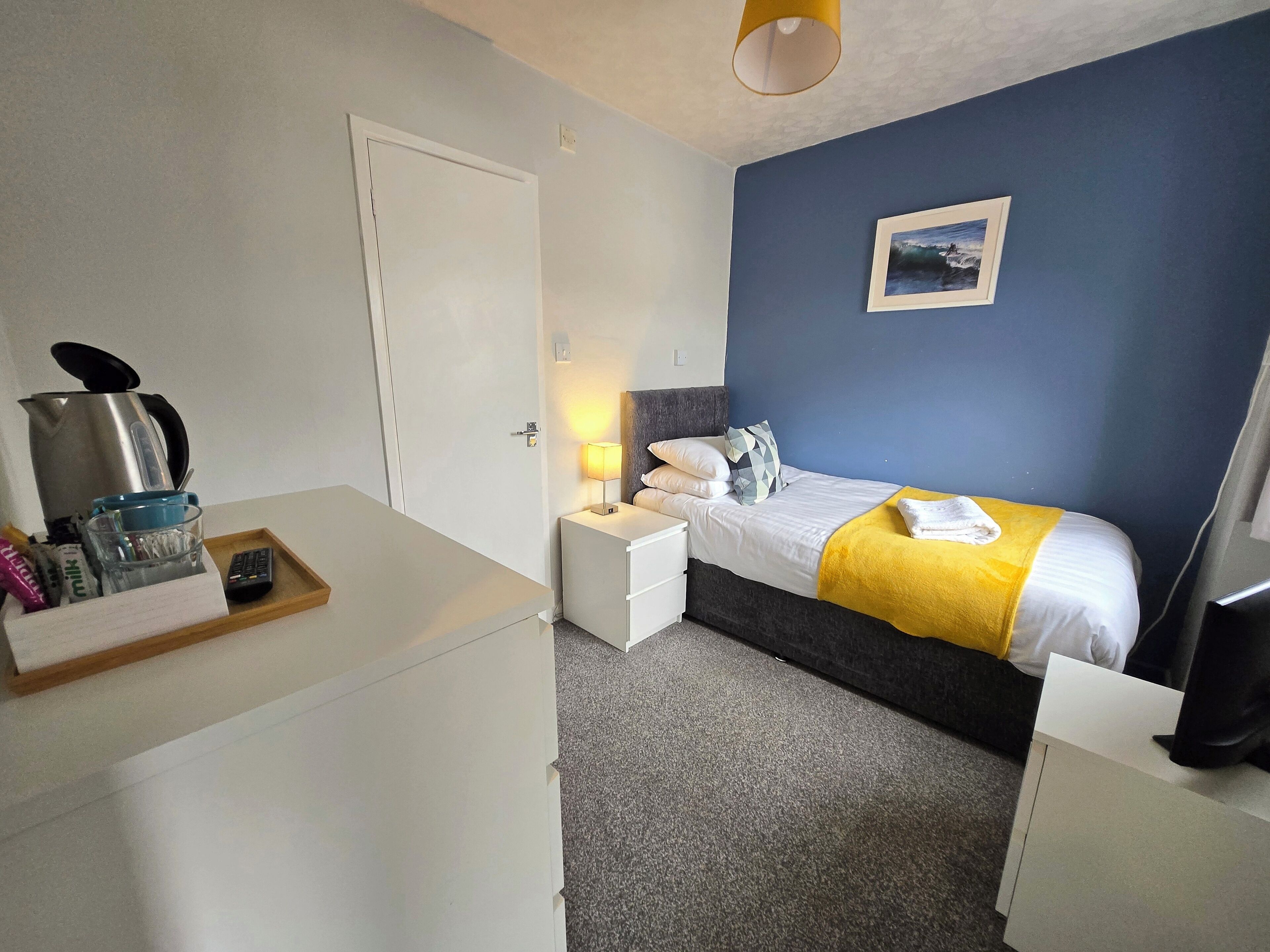 Una camera da letto con un letto, un comodino, una lampada e un quadro appeso al muro.
