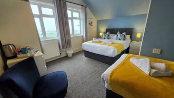 A hotel room with a bed, a chair, a desk with a kettle, and a window with curtains.